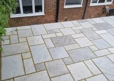 Riven sandstone paving laid beneath a brick wall